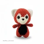 A small handmade crochet red panda doll with red and white fur, large black eyes, and a black belly.